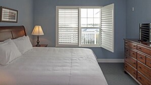 A bedroom with a large bed, a nightstand with a lamp, a dresser, and a window with blinds. - RBC 2 Heritage Golf Week 2-BR resort Hilton Head Island - AC, WiFi, fitness room (Hilton Head Island)