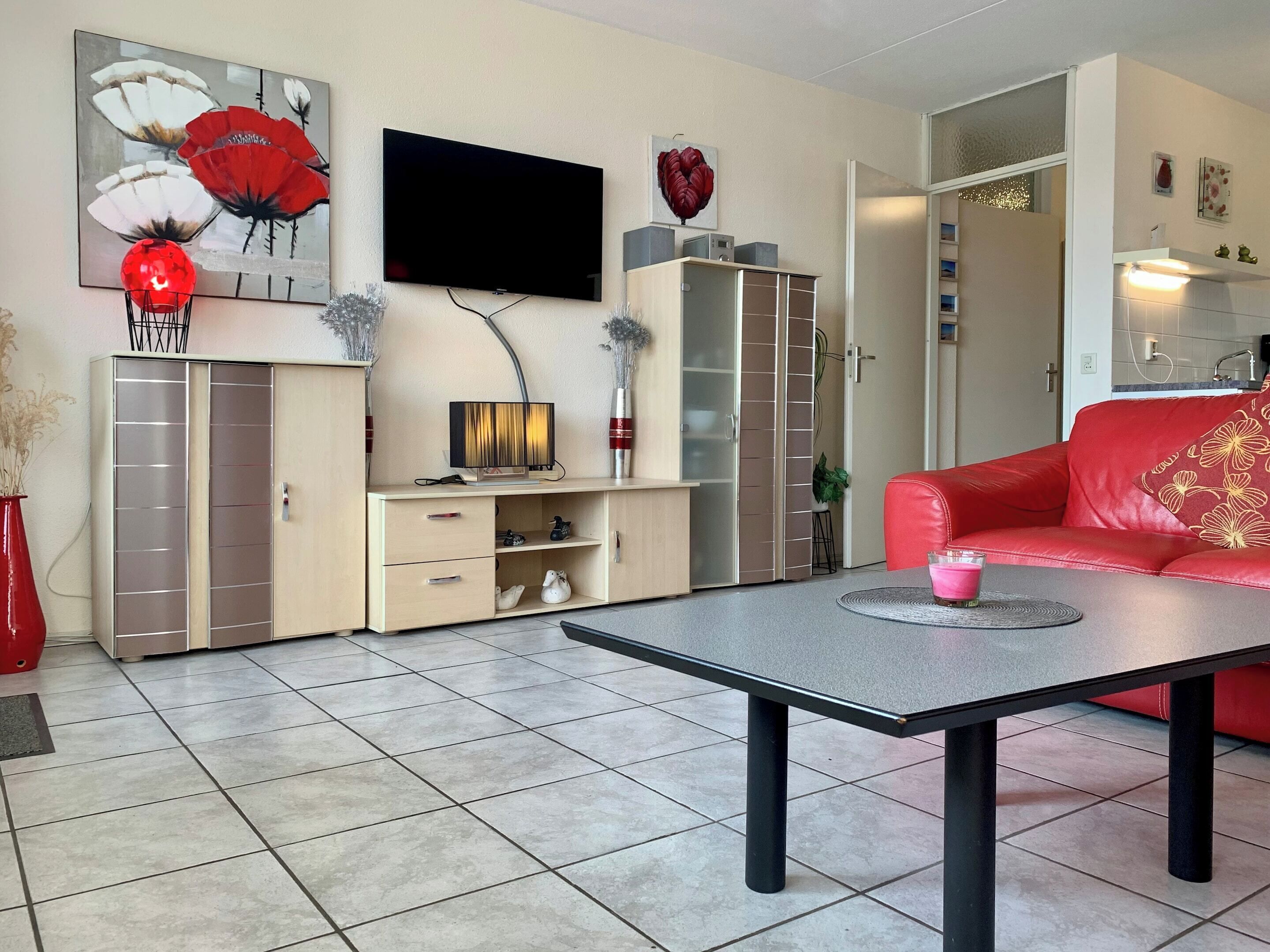 Un salon moderne avec un téléviseur à écran plat, un canapé rouge, une table basse et un meuble avec des tiroirs.