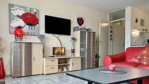 Un salon moderne avec un téléviseur à écran plat, un canapé rouge, une table basse et un meuble avec des tiroirs.