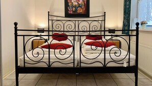 Un lit à baldaquin avec une structure en métal noir et du linge de lit blanc, un tableau au-dessus de la tête de lit et une fenêtre avec des rideaux sur le côté droit.