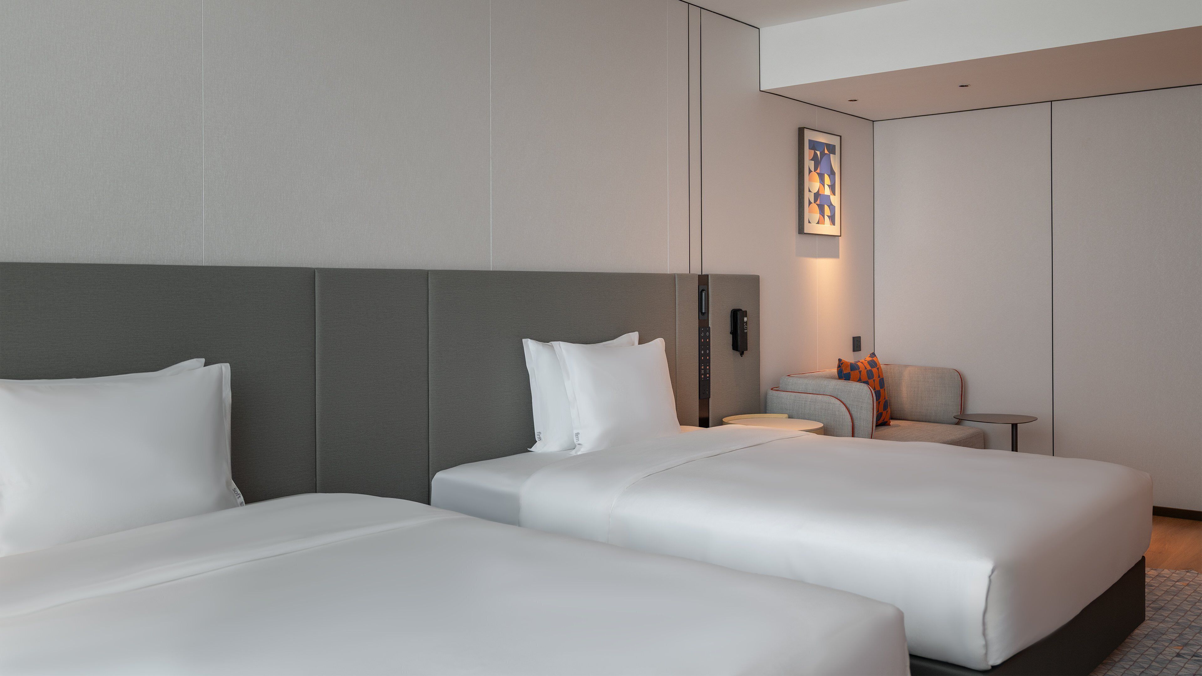 A hotel room with two beds, a small table, a chair, and a wall-mounted phone.