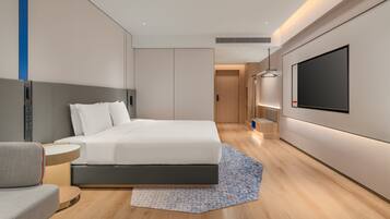 Una habitación de hotel moderna con cama, mesita de noche, televisor y un pequeño rincón de descanso.