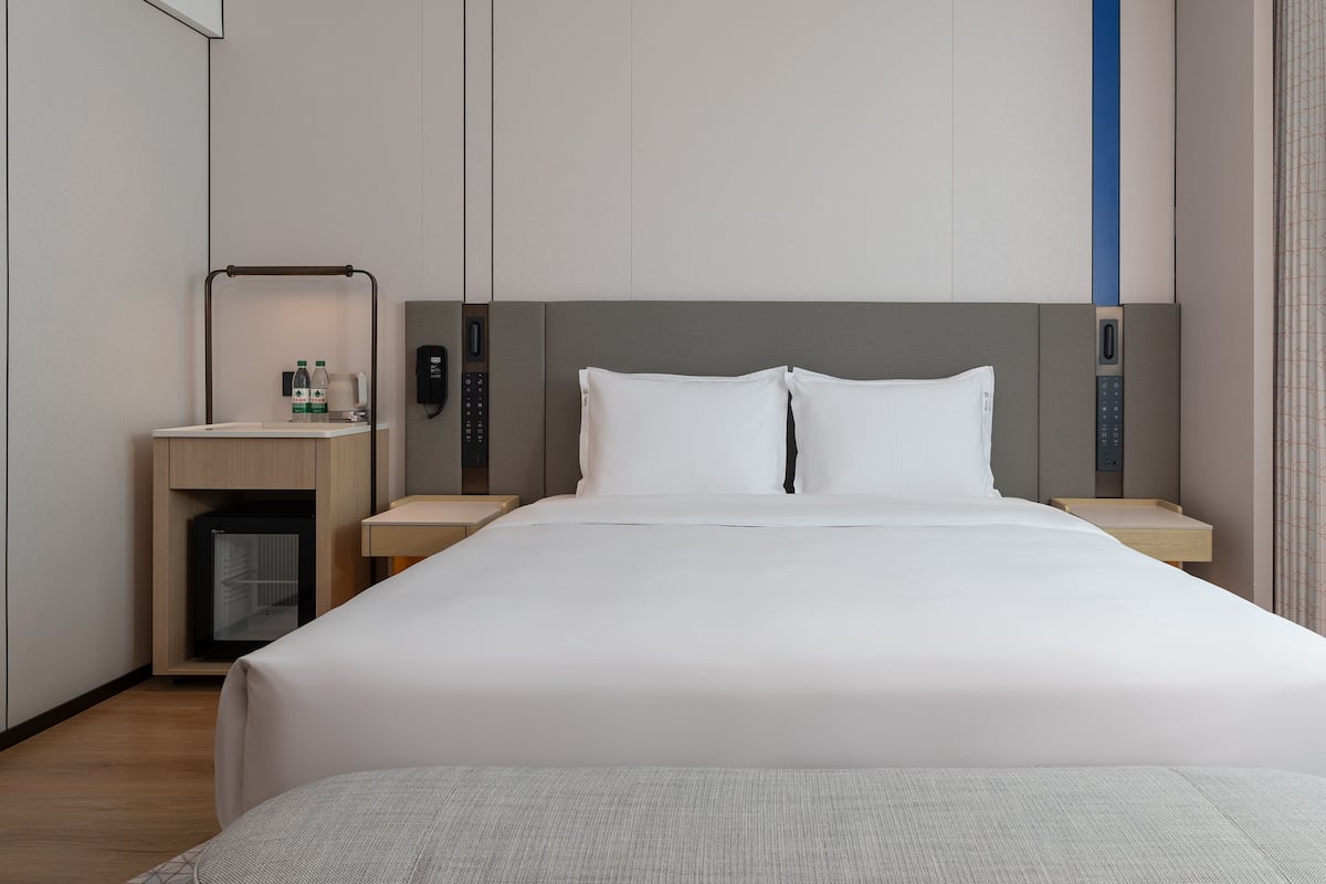 A hotel room with a bed, bedside tables, a desk, a mirror, and a phone.