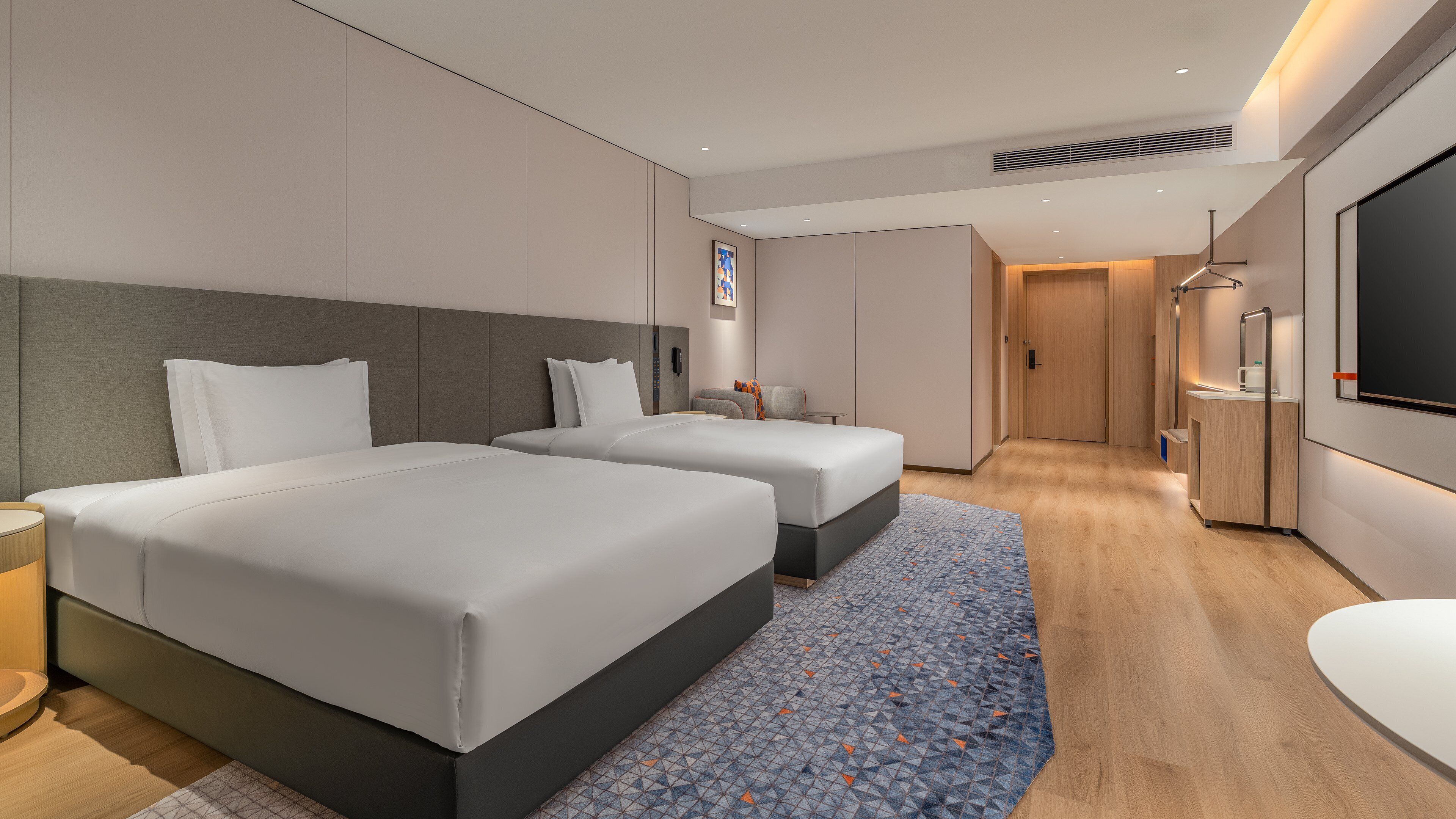 A hotel room with two beds, a desk, a TV, and a bathroom.