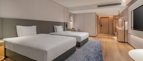 A hotel room with two beds, a desk, a TV, and a bathroom.