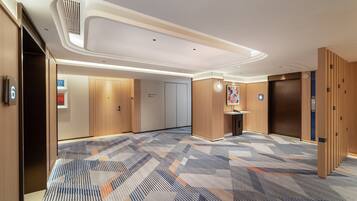 Un couloir d’hôtel avec un tapis à motifs, des portes en bois, une petite table avec un téléphone et un ascenseur.