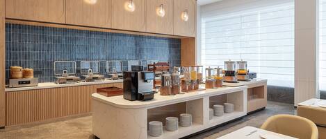 A modern breakfast bar with coffee machines, a seating area, and a view of the outdoors.