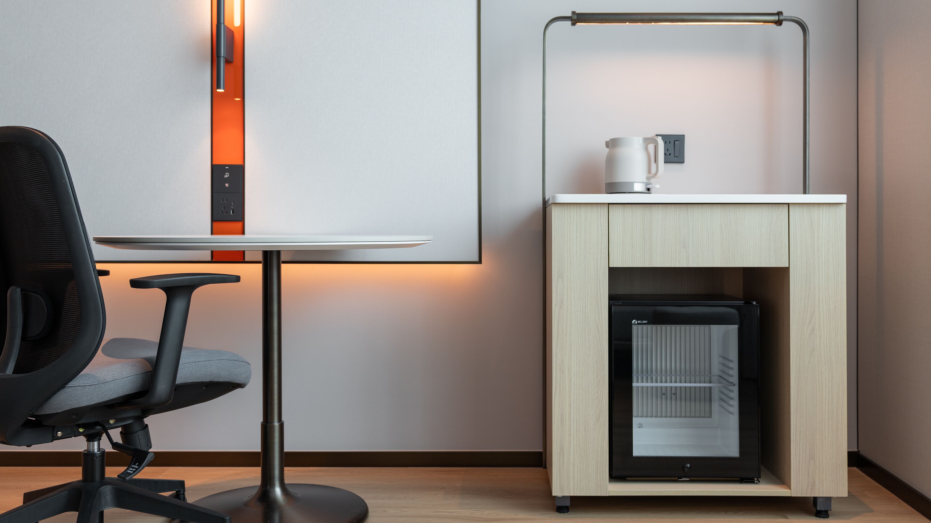 A modern hotel room with a desk, chair, and a minibar.