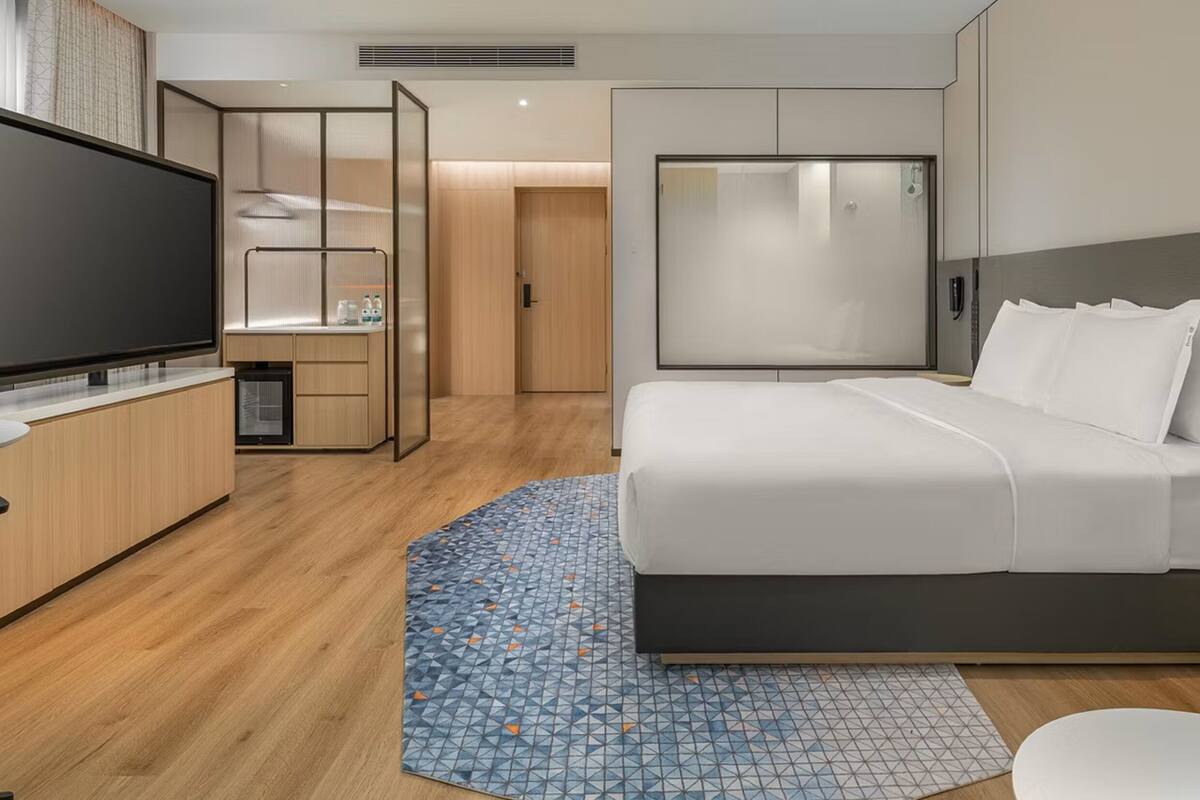 A modern hotel room with a bed, a TV, a desk, and a wardrobe.