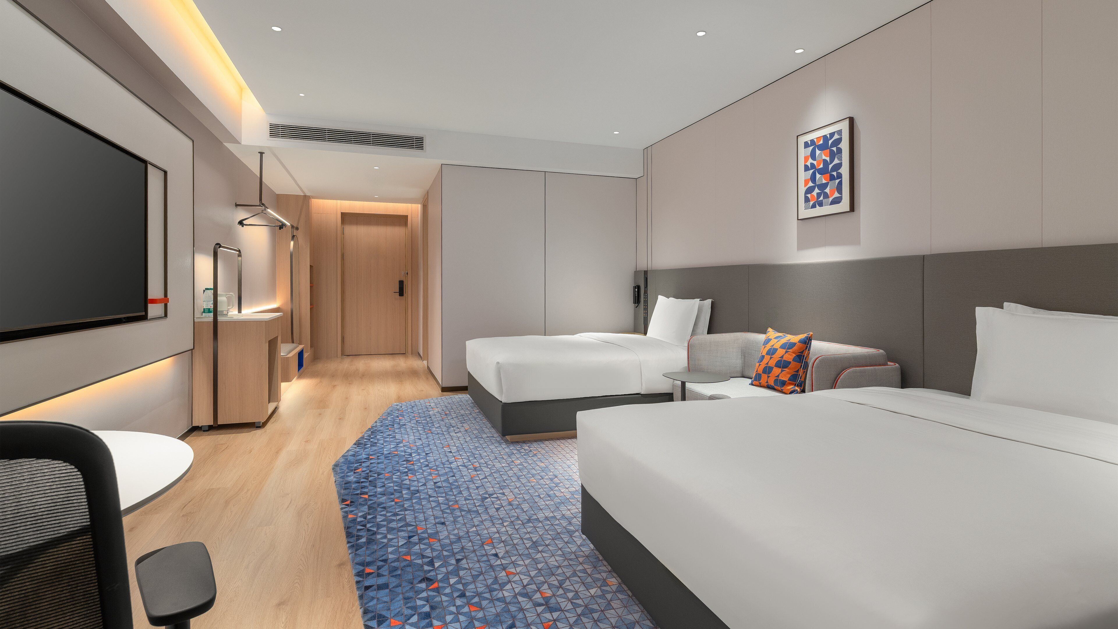 A modern hotel room with a large bed, a smaller bed, a desk, and a seating area.