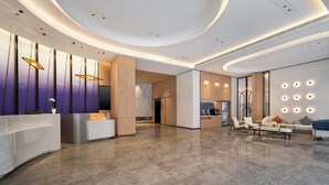 Um lobby moderno com balcão de recepção, área de estar e uma parede com luminárias circulares.