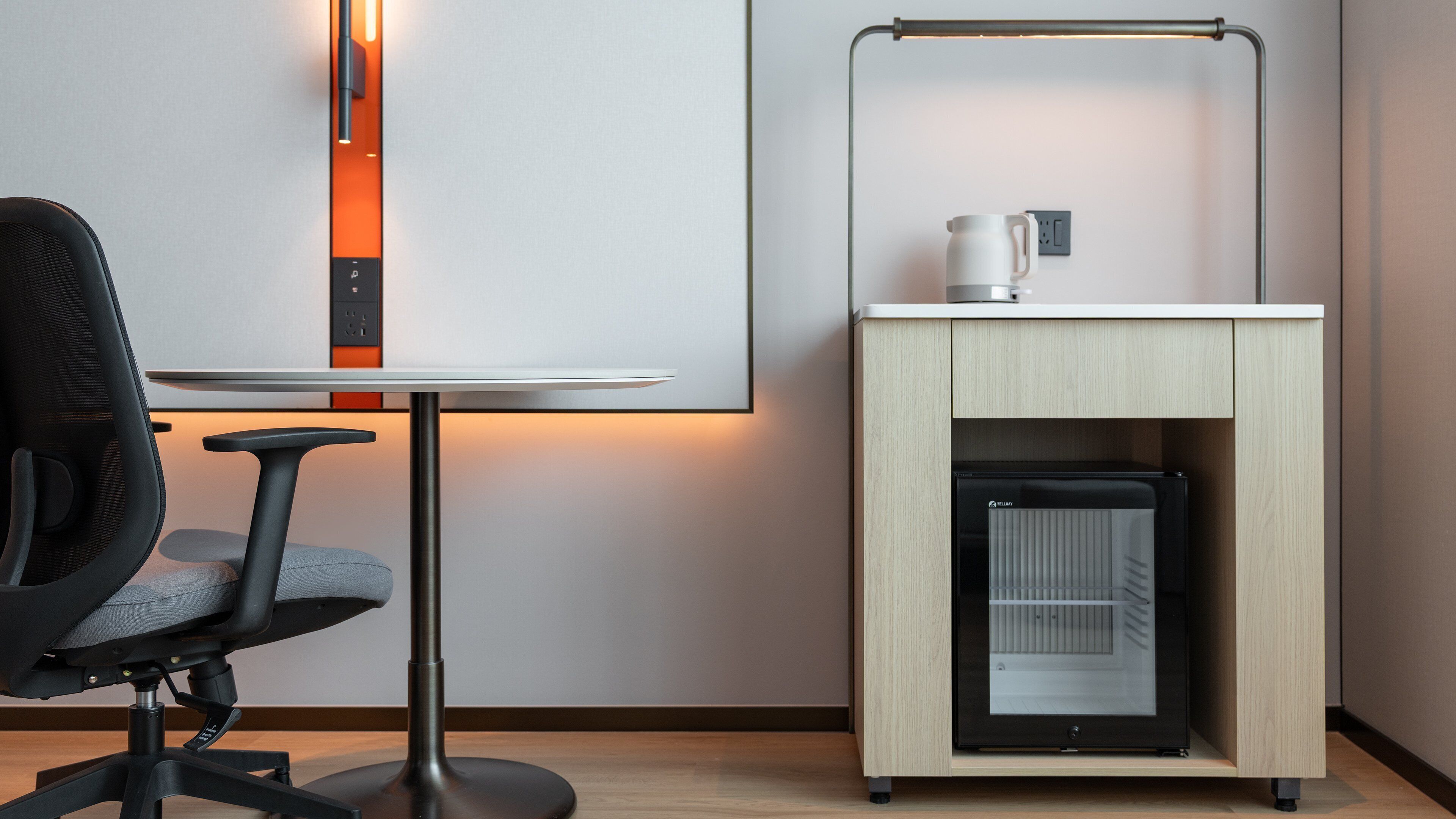 Un espacio de oficina moderno con un escritorio, una silla y una pequeña zona de kitchenette con un refrigerador y una cafetera.