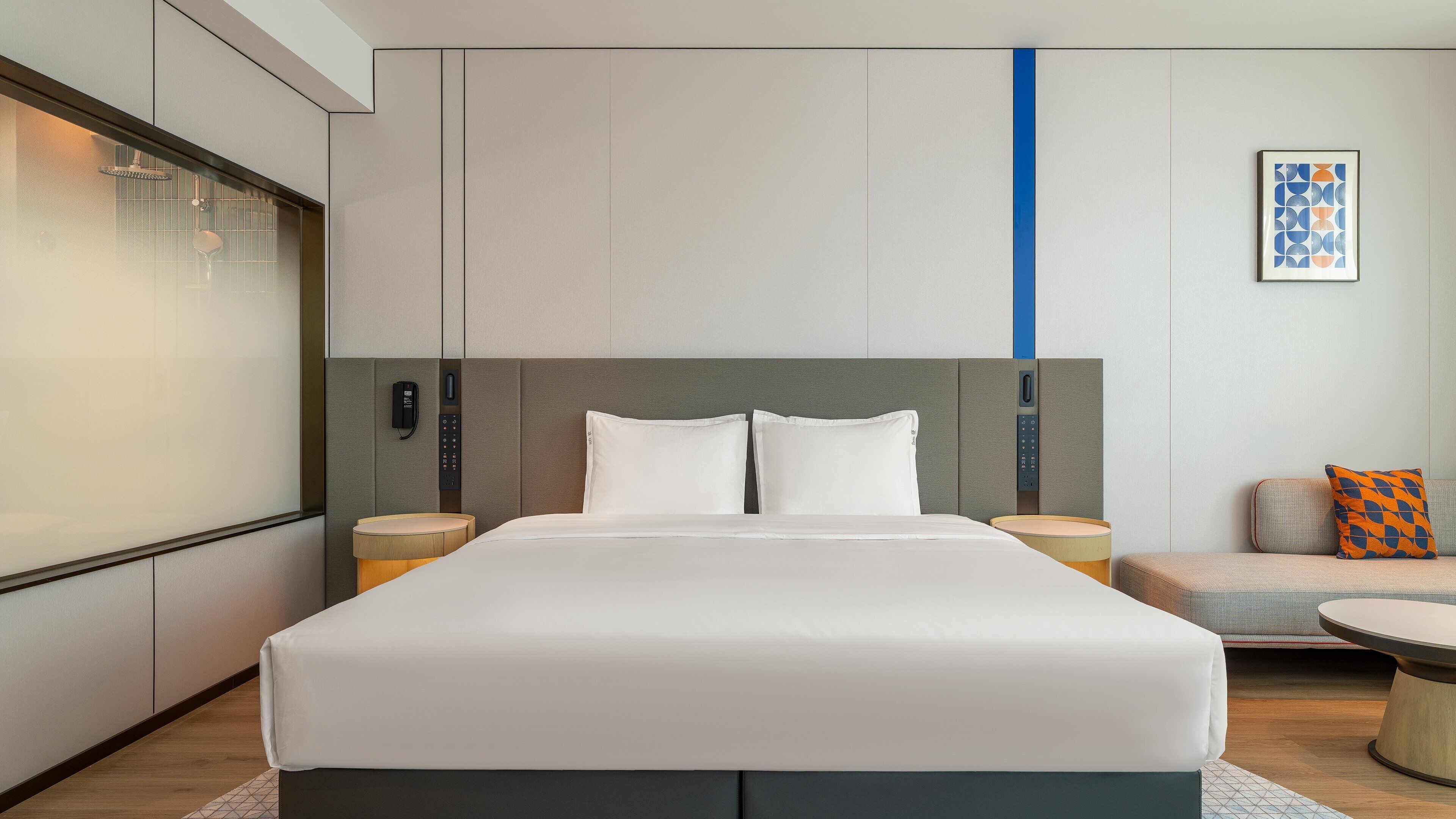 A modern hotel room with a large bed, bedside tables, a sofa, and a wall-mounted phone.