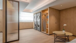 A modern laundry room with built-in washers and dryers, a wooden floor, and a small table with a vase.