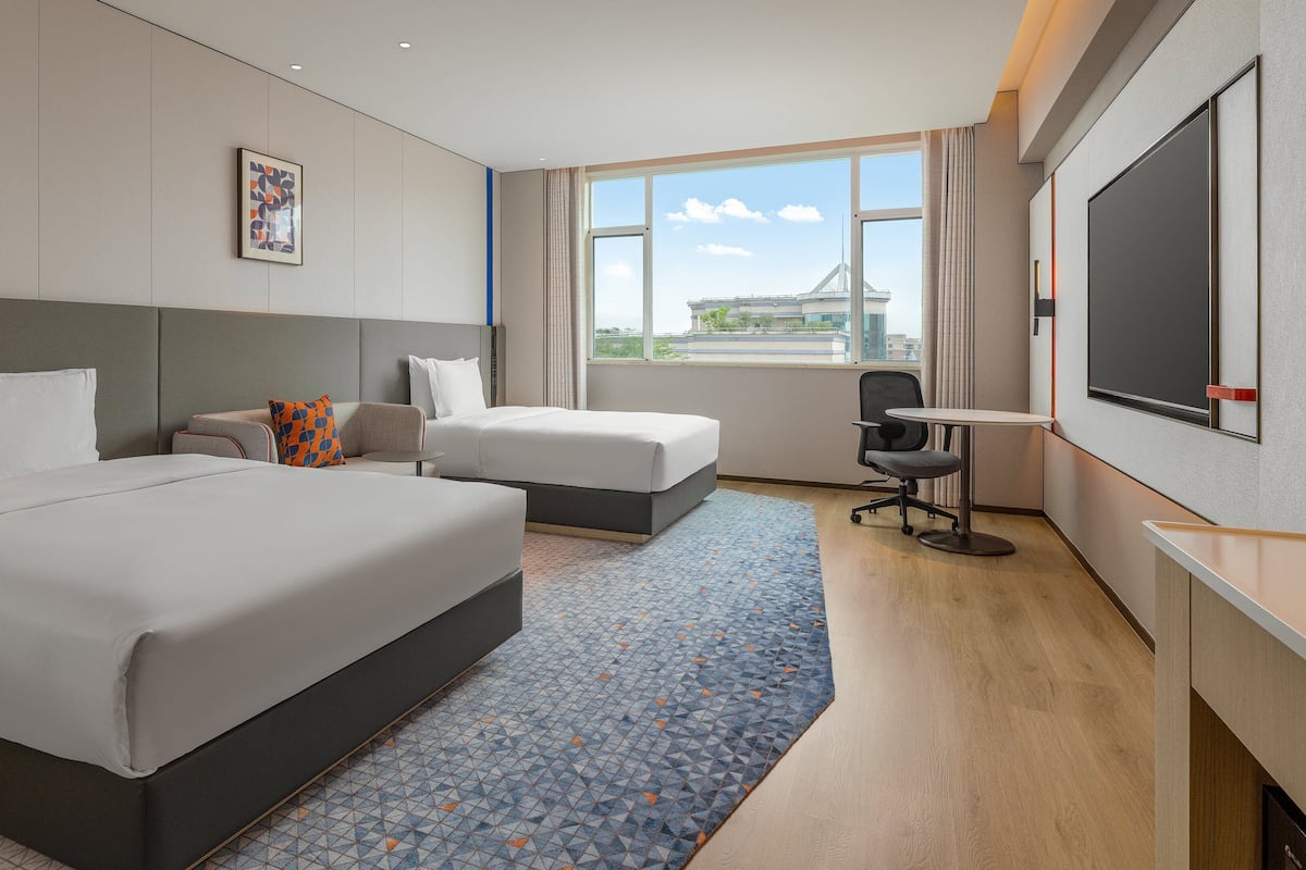 A hotel room with a large bed, a smaller bed, a desk, and a TV.