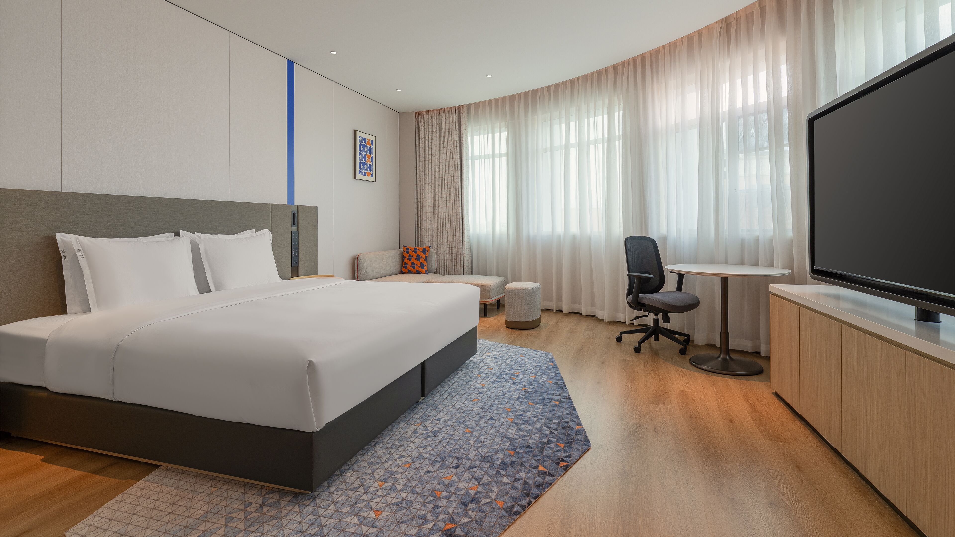 Una habitaci ón de hotel moderna con una cama grande, un escritorio, una silla, un televisor y una ventana con cortinas.