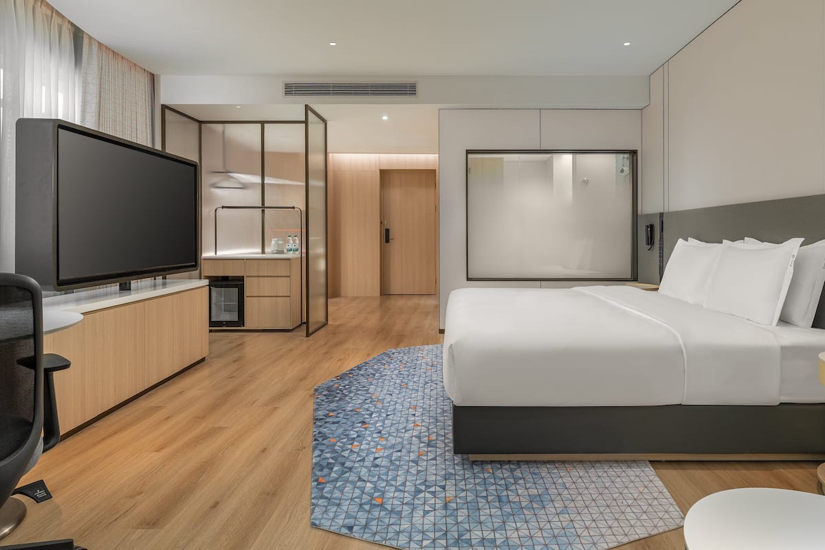 A modern hotel room with a large bed, a TV, a desk, and a walk-in closet.