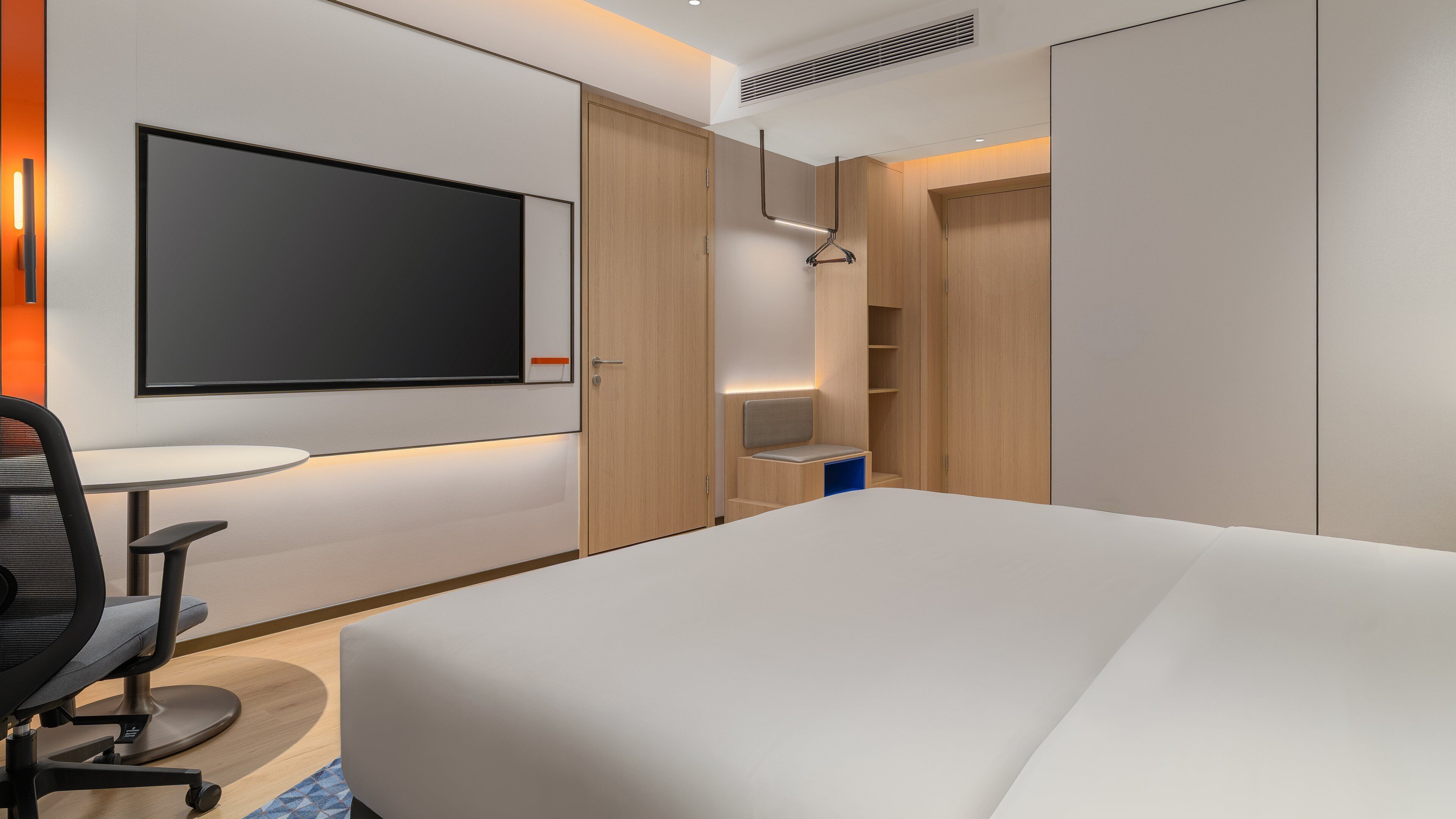 Habitación de hotel moderna con una cama grande, un escritorio con silla, televisor y estanterías integradas.