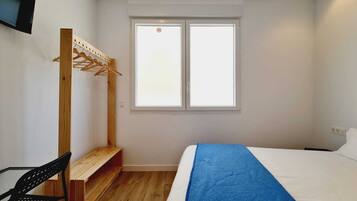 A bedroom with a bed, a wooden bench, a chair, a window, and a wall-mounted drying rack.