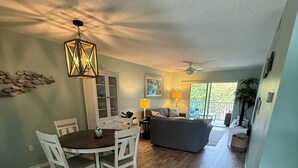 A spacious living area with a dining table and chairs, a sofa, a ceiling fan, and a view to an outdoor balcony. - Island Time - 2 Minute Walk To The Beach & Heated Pool (Holmes Beach)