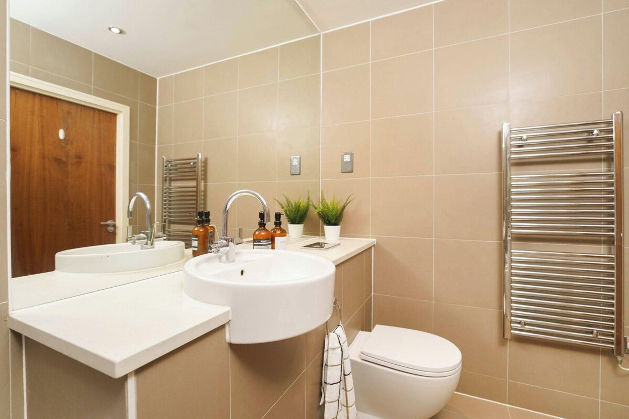A modern bathroom with two sinks, a toilet, a towel rack, and a mirror.