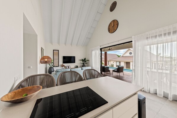 Una cocina moderna con una isla grande, un comedor con sillas de mimbre y vista a una piscina.