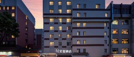 A multi-story hotel with illuminated signage, a ground-level retail area, and a clear sky.