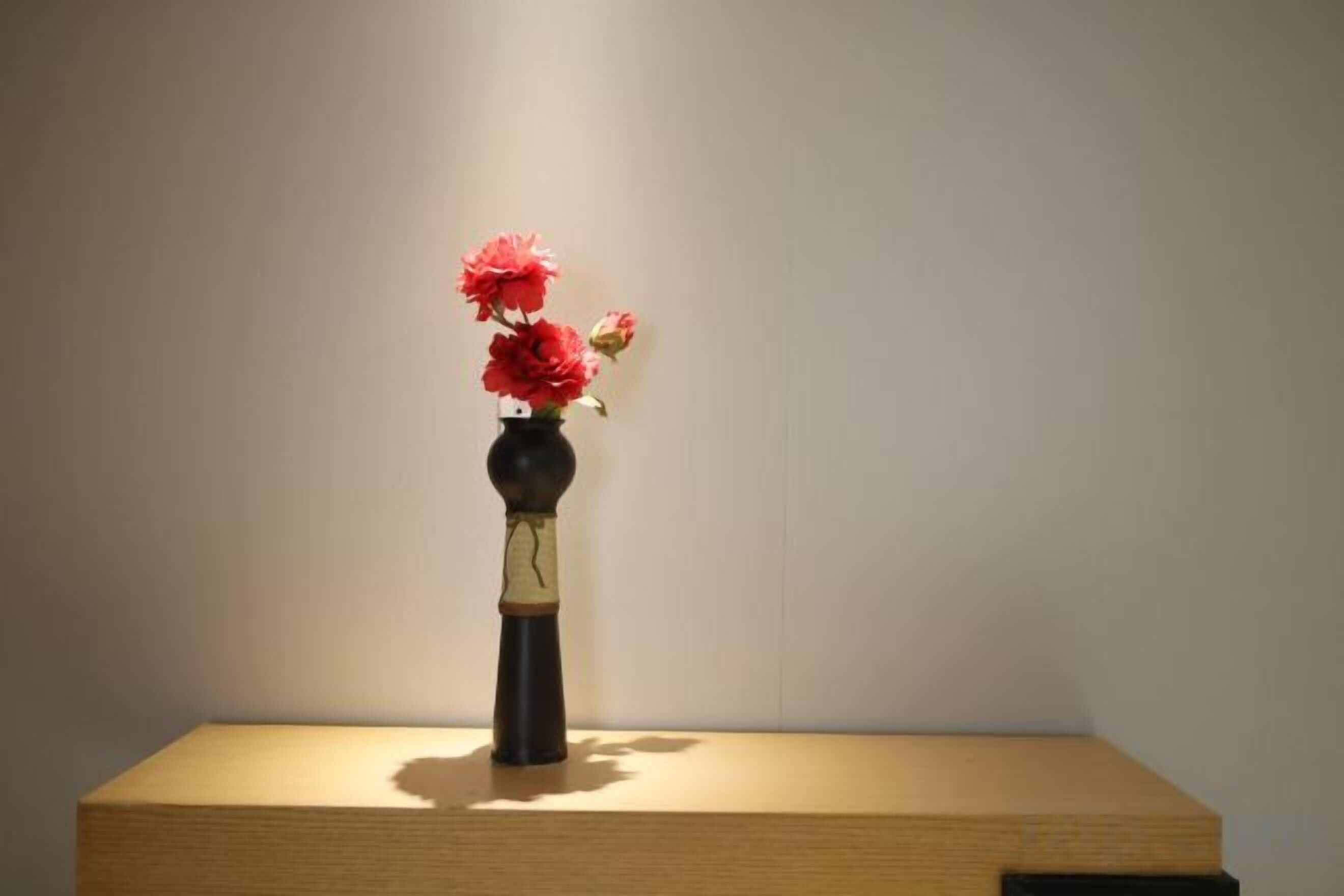 Een vaas met bloemen op een houten plateau voor een effen muur.