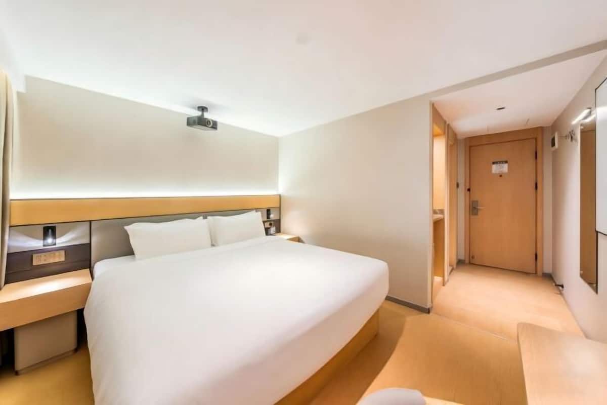 A hotel room with a large bed, bedside tables, a nightstand, a headboard, and a door leading to another room.