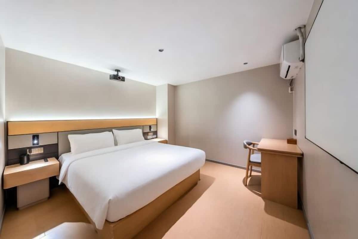 A modern hotel room with a large bed, bedside tables, a desk, and a wall-mounted air conditioning unit.