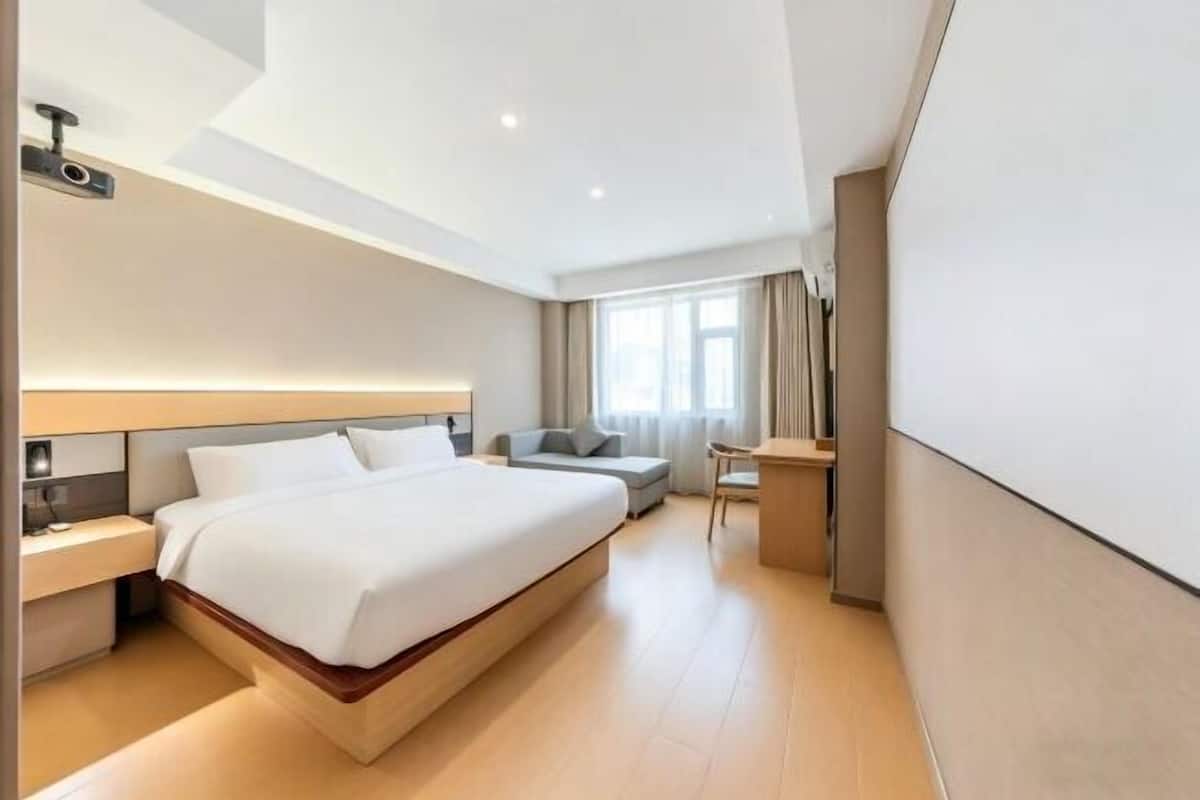 A modern hotel room with a large bed, a desk, a chair, and a sofa.