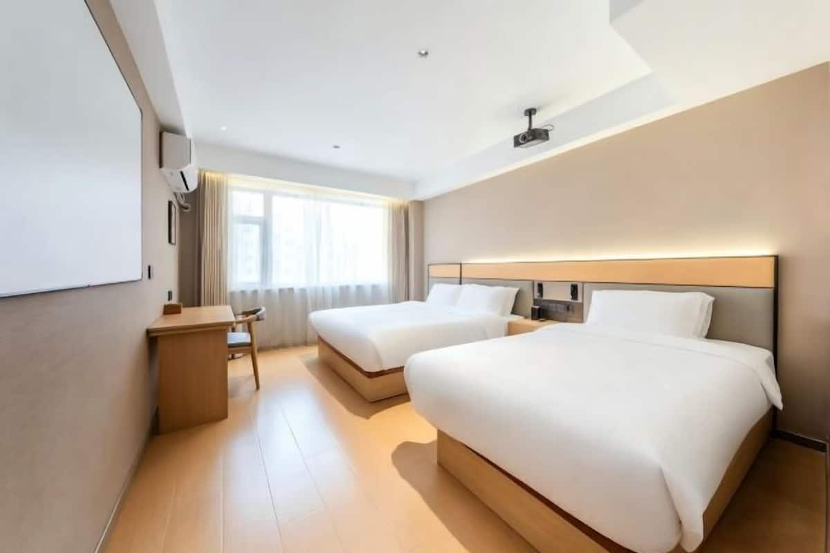 A hotel room with two beds, a desk, a chair, and a large window.