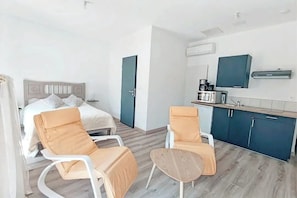 Ein modernes Hotelzimmer mit einem Bett, zwei Stühlen, einem kleinen Tisch, einer Küchenzeile und einem Fernseher.