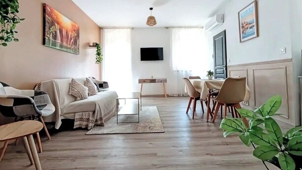 Un salon moderne comprenant un canapé, une table basse et un coin repas. Un téléviseur est fixé au mur et une fenêtre laisse entrer la lumière naturelle.
