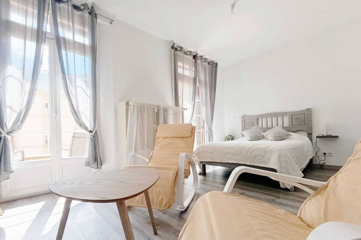 A bedroom with a bed, a chair, a table, and a window with curtains.
