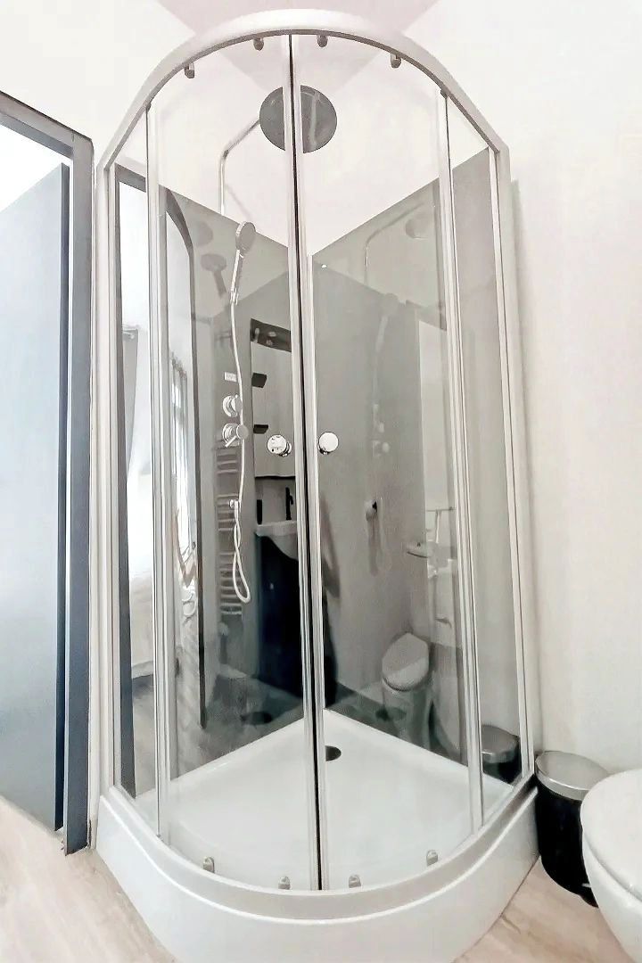 Un box de ducha con mampara de vidrio, un asiento integrado y un cabezal de ducha de mano.