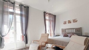 Une chambre à coucher avec un lit, deux chaises, une table de chevet et une fenêtre avec des rideaux.