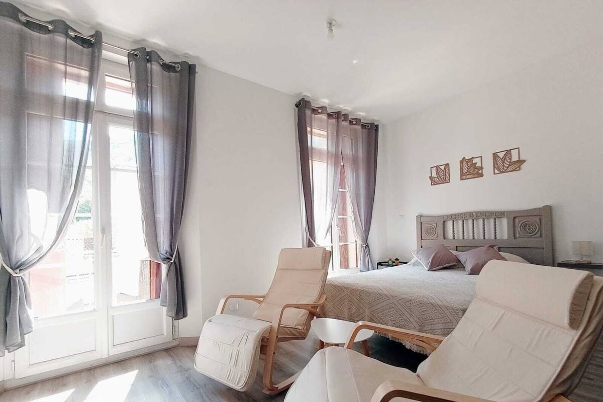 A bedroom with a bed, two chairs, a nightstand, and a window with curtains.