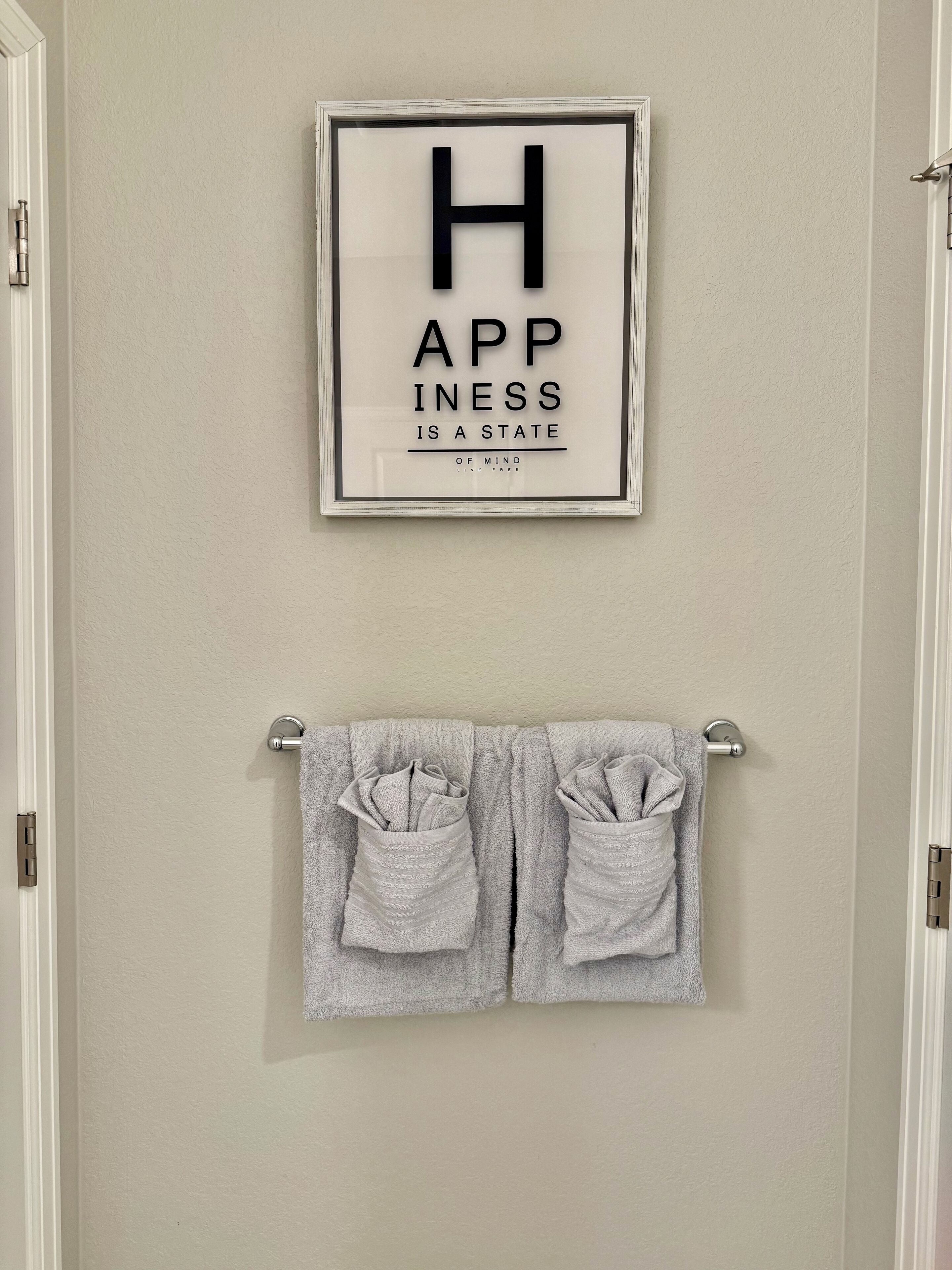 A framed quote on a wall and a towel rack with two folded towels.