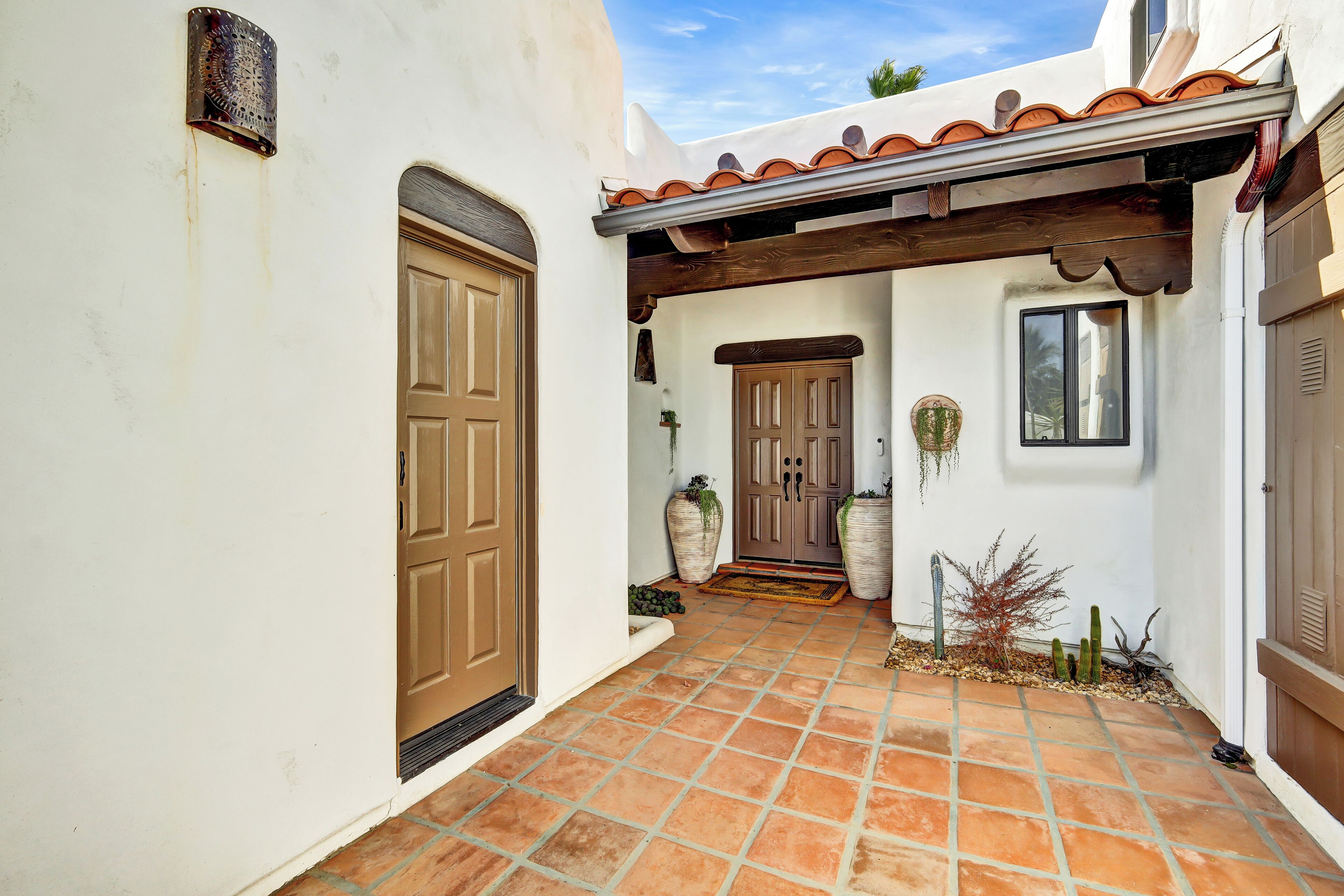 A courtyard with a tiled floor, a wooden door, and a covered entrance.