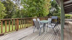 A wooden deck with a glass-top table and chairs, a grill, and a wooden railing. - Birdstow – Spacious, peaceful Stay, Sleeps 10 (Wentworth Falls)