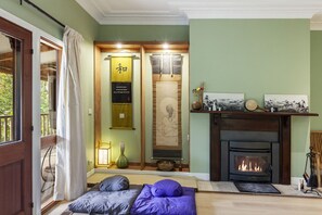 A cozy room with a fireplace, a bed with pillows, a hanging scroll, and a small table with a lamp. - Birdstow – Spacious, peaceful Stay, Sleeps 10 (Wentworth Falls)