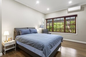 A bedroom with a bed, nightstands, a window with a view of greenery, and an air conditioning unit. - Birdstow – Spacious, peaceful Stay, Sleeps 10 (Wentworth Falls)