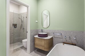Een badkamer met een glazen douchecabine, een wit toilet, een houten wastafelmeubel met een paarse wasbak, een vrijstaand bad en een spiegel aan de muur.