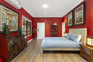 A bedroom with red walls, a wooden bed, a dresser, and artwork.