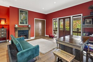 A room with a fireplace, a teal sofa, a wooden dining table, and a view of a garden through glass doors.