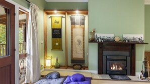A cozy room with a fireplace, a bed with pillows, a hanging scroll, and a small table with a lamp. - Sakura – Calm, Cozy, & Close to Nature (Wentworth Falls)