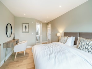 A bedroom with a bed, bedside table, chair, and a bathroom visible through an open door.