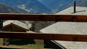 A mountain view from a wooden balcony with snow-capped peaks in the background.