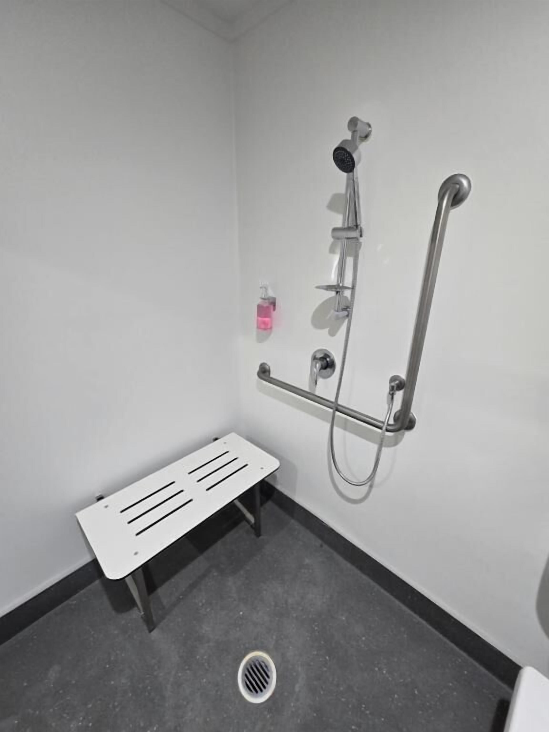 Un baño pequeño y moderno con ducha, un banco y un secador de manos.